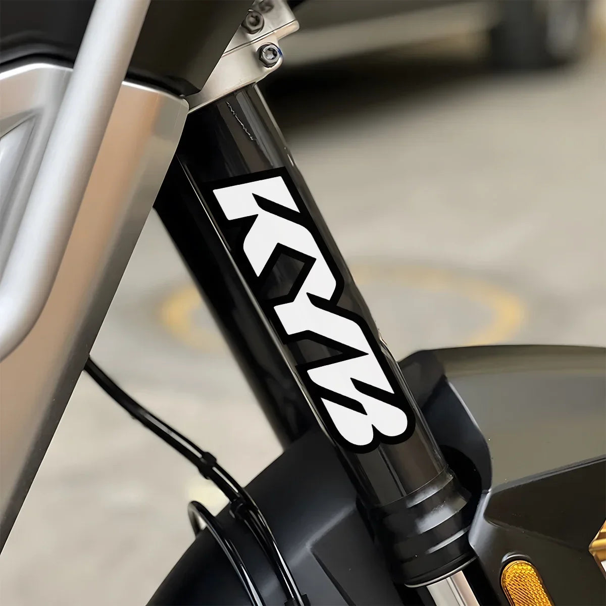 Close-up of a black motorcycle suspension fork with white KYB decals on the lower shaft.