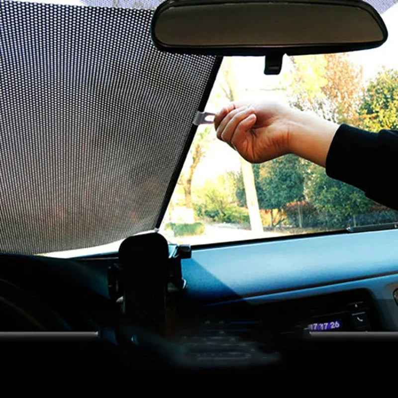 A hand is opening a retractable car windshield sun shade inside a vehicle.