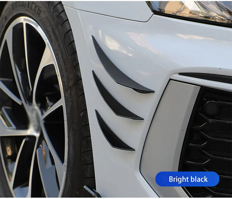 Close-up of bright black universal car spoiler fins installed on a white car's front bumper near the wheel.