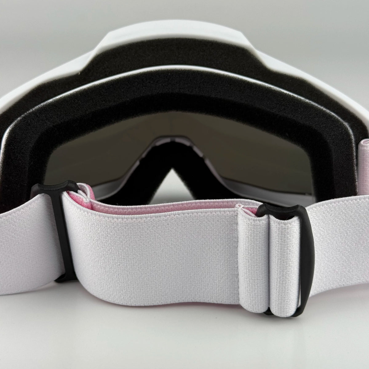 White and black off-road motorcycle goggles with a pink strap shown in a close-up view.