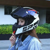 A woman wearing a black and white racing-style motorcycle helmet outdoors.