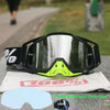 A pair of black and neon yellow motocross goggles resting on a white cloth with a blue outline.