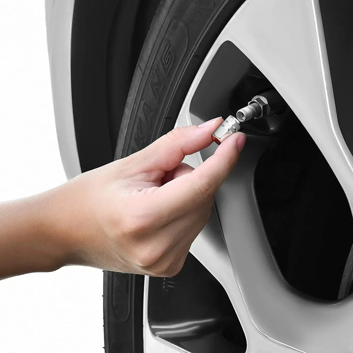 A hand is inserting a durable aluminum valve cap onto a tire valve stem of a wheel.