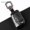 A black carbon fiber button cover for a car key, featuring a silver clip and colored accent.