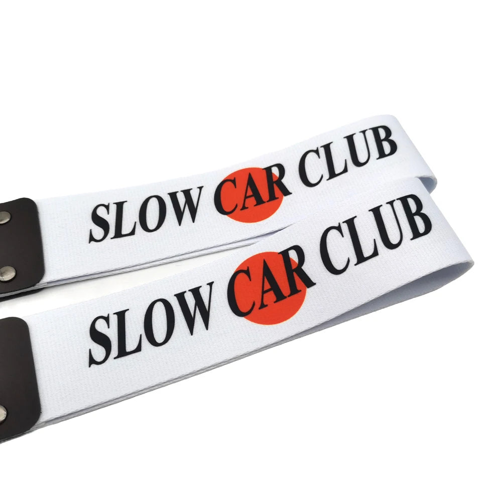 Two white silicone tow straps with black hardware featuring the text Slow Car Club and an orange circle logo