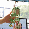 A hand holds a strawberry crochet hanging decor made of green yarn against a blurred background.