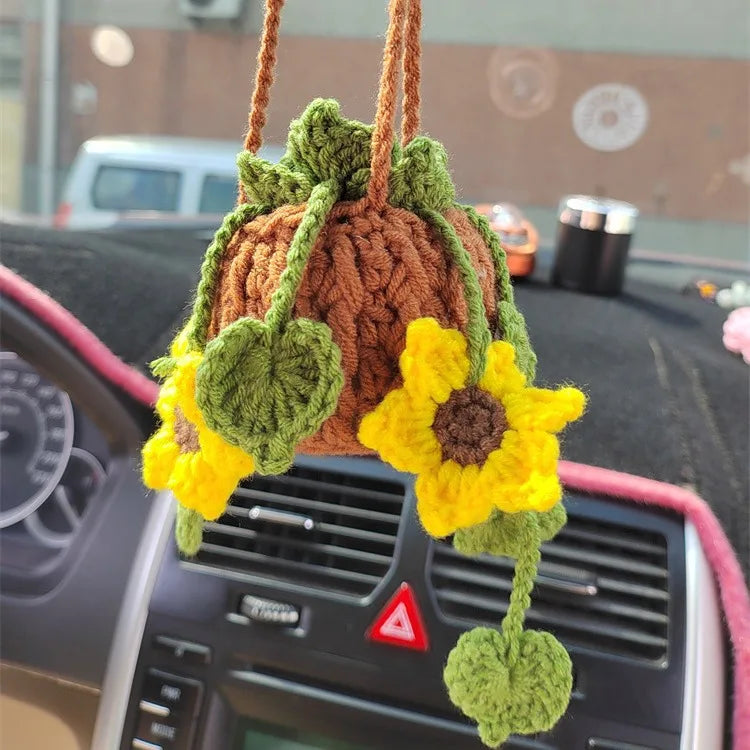 A strawberry crochet hanging decor made of brown and green yarn is displayed on a car dashboard.