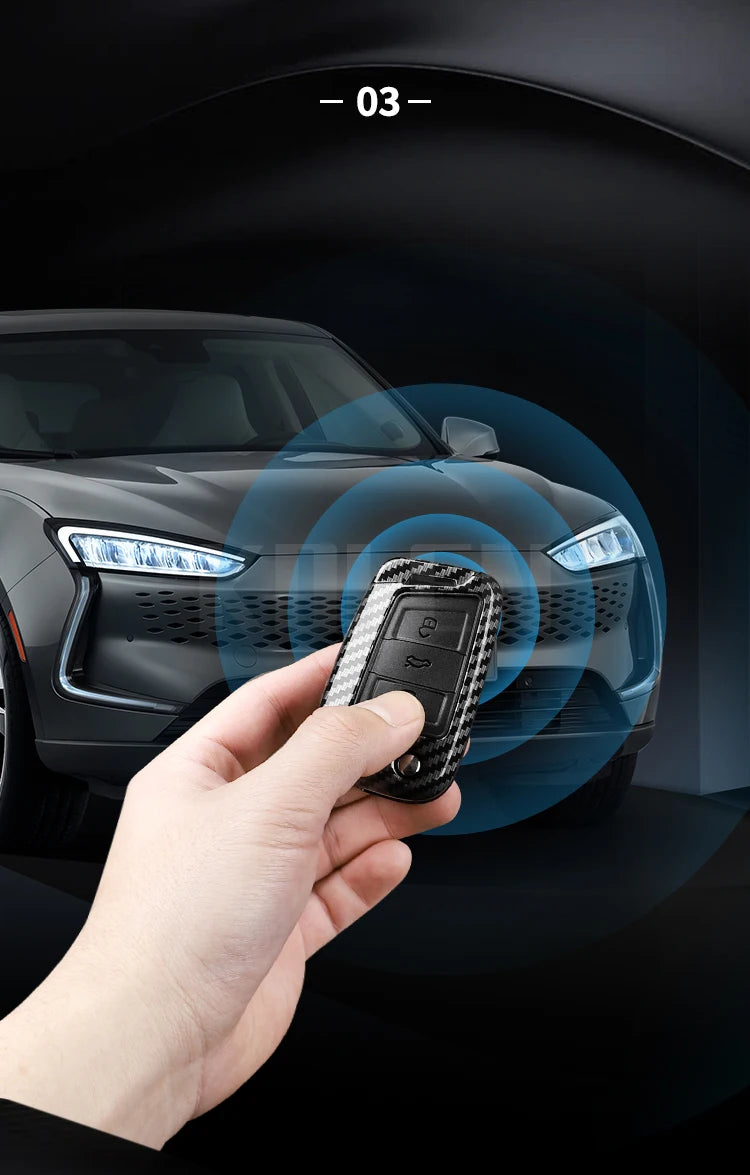 A hand holds a carbon fiber button cover for a car key, positioned in front of a modern vehicle's headlight.