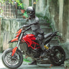 A person wearing a black helmet sits on a red Ducati motorcycle with a black fanny pack.