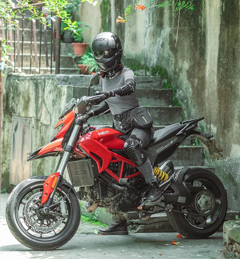 A person wearing a black helmet sits on a red Ducati motorcycle with a black fanny pack.