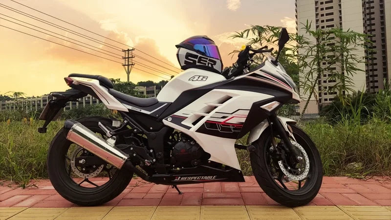 A white and black motorcycle with a clear visor is parked outdoors against a sunset backdrop.