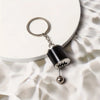 A silver keychain with a black cylindrical charm and a spherical bead rests on a white surface.