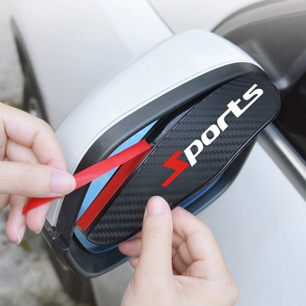 A hand is holding a black and gray car rearview mirror rain protection accessory with a red stripe and 'sports' text.