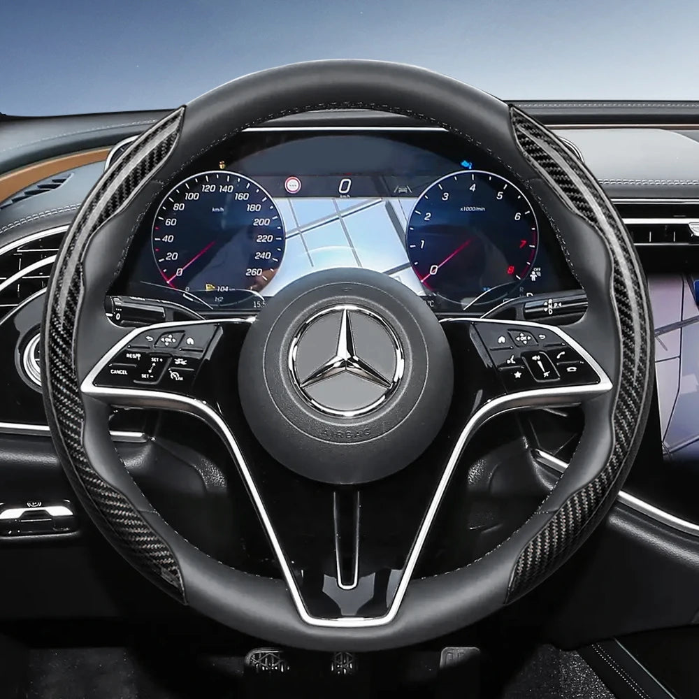 Close-up view of a black steering wheel with carbon fiber texture covers and a Mercedes-Benz logo.