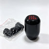 A black gear shift knob with red markings 135 HH 246R is shown next to a clear plastic bag containing several black gear shif