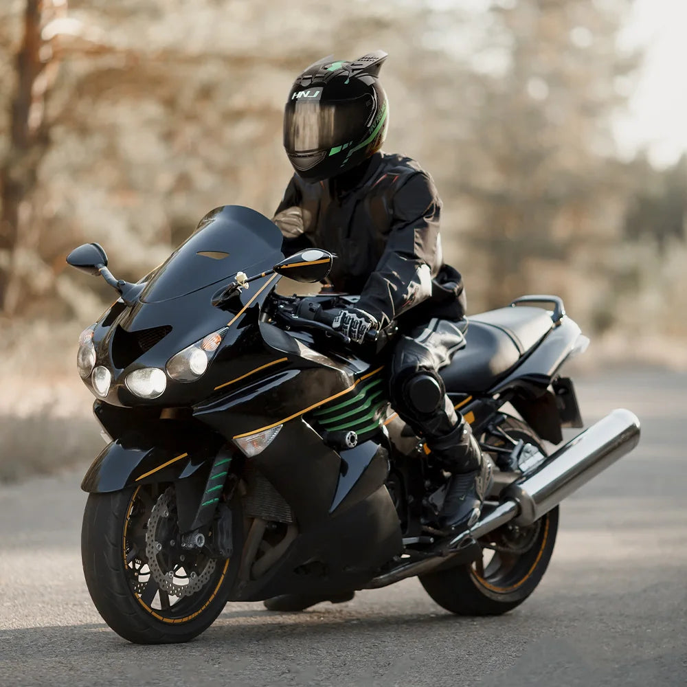 A person wearing a black full face motorcycle helmet is riding a black sport bike on an asphalt road.
