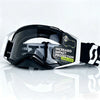 A pair of black and white safety goggles with a lens lock feature resting on a reflective surface.
