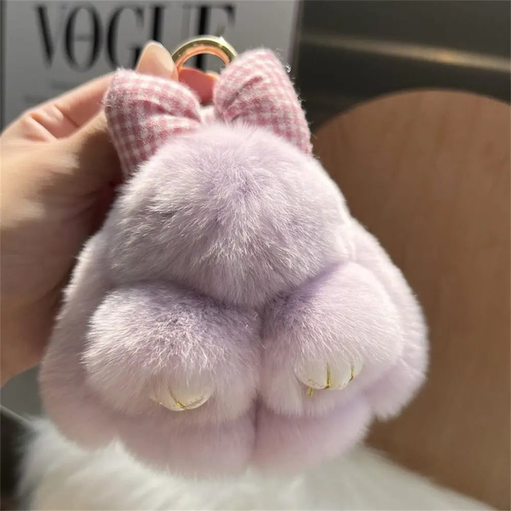 A soft lavender plush bunny keychain with pink fur and a gold ring is being held by a hand.