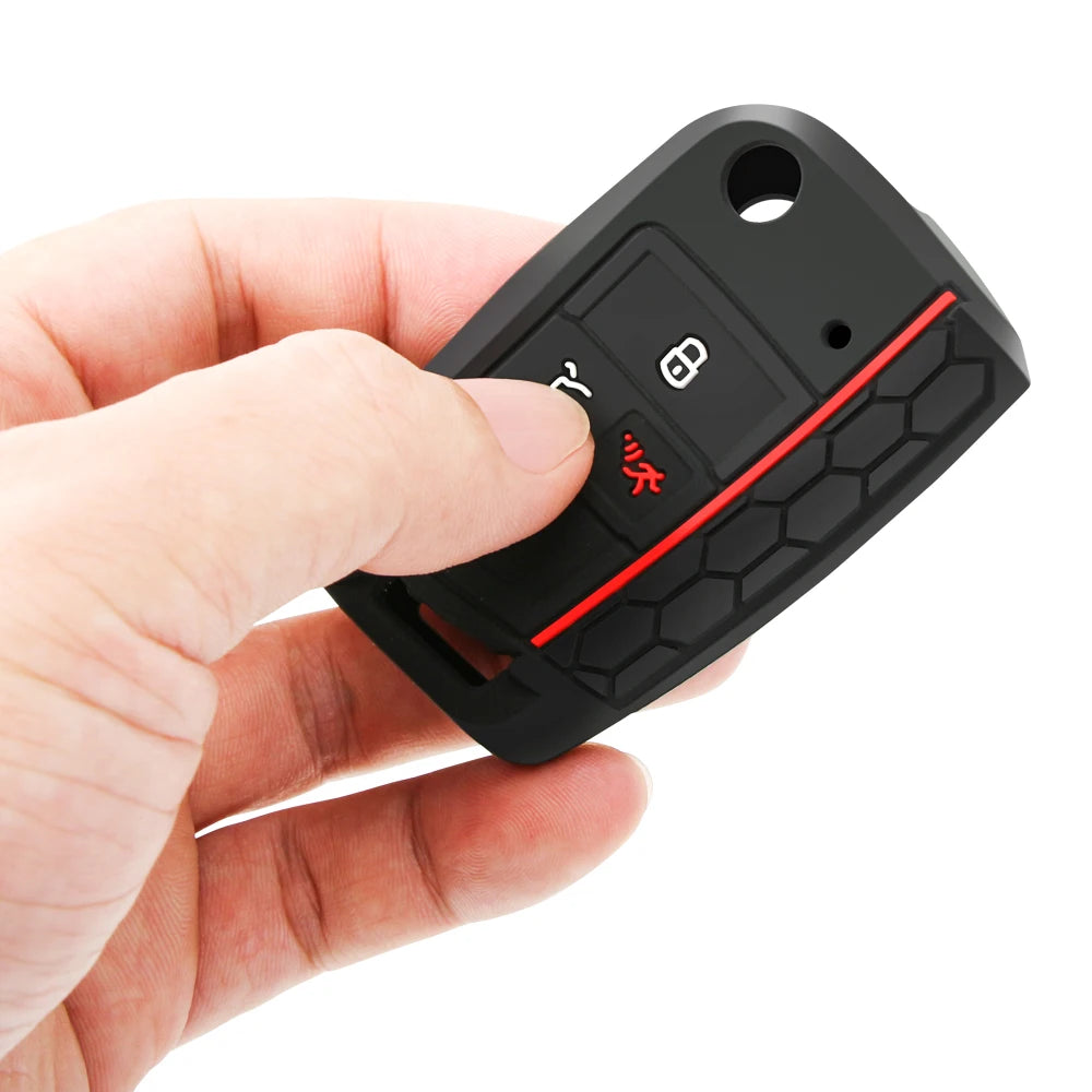 A hand holds a black silicone car key cover with a red accent, showing the key slot and a button.