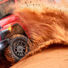 Un Jeep rouge soulève un grand nuage de poussière orange sur un terrain sablonneux.