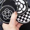 A hand holds a set of two black and white patterned silicone car cup coasters with silver glitter edges.