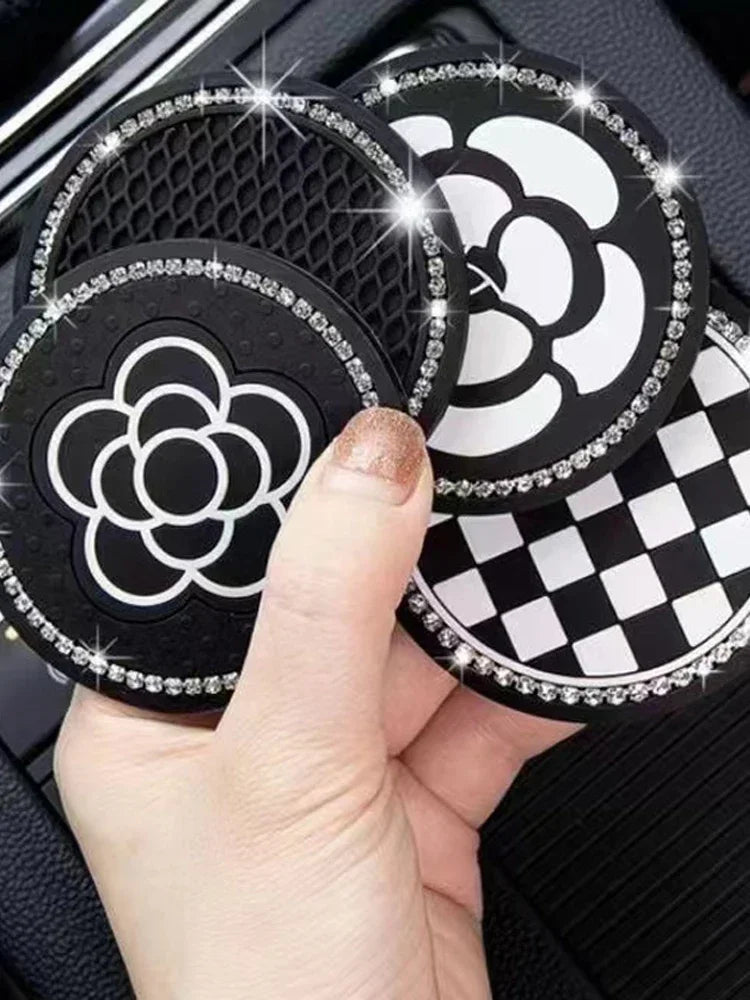 A hand holds a set of two black and white patterned silicone car cup coasters with silver glitter edges.