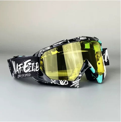 Un par de gafas de motocicleta negras y amarillas con lente transparente, apoyadas en una superficie gris.