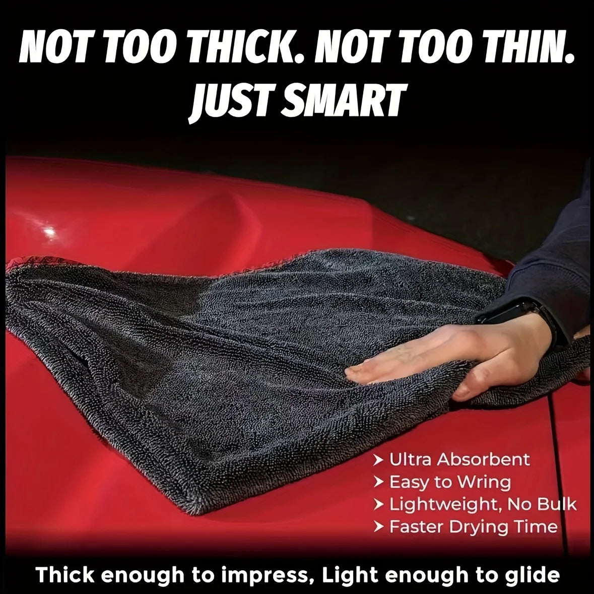 A dark gray microfiber drying towel is shown draped over a red surface, emphasizing its thinness and absorbency.