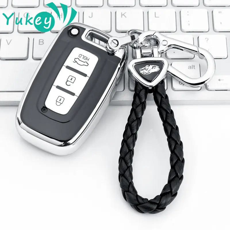 A silver car key case with a black leather cord attached, resting on a white laptop keyboard.