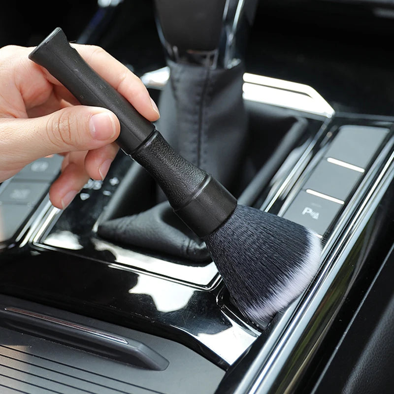 Une main tient une brosse de detailing noire à poils doux, positionnée sur la surface de l'intérieur d'une voiture.
