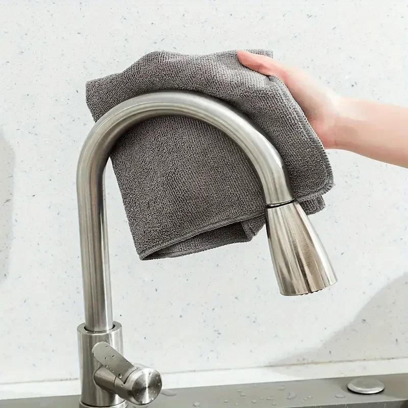 Eine Hand hält ein graues Mikrofasertuch über einen Edelstahl-Küchenwasserhahn.