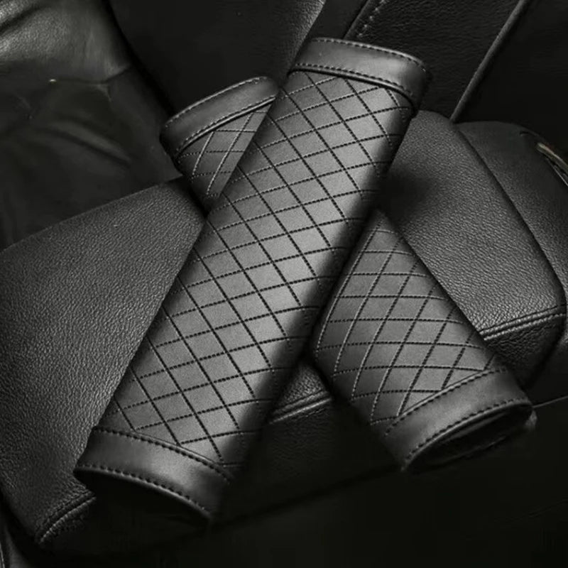 A close-up of two black PU leather car seat belt covers folded and laid diagonally on a dark surface.