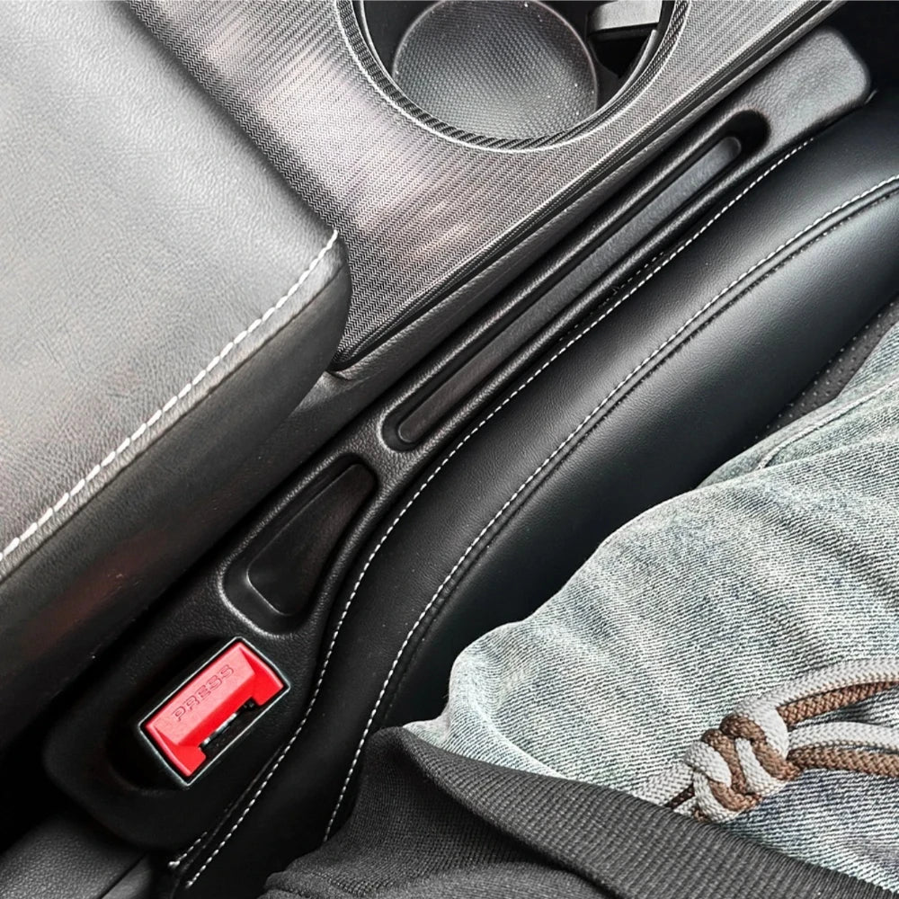 A black car seat gap filler organizer with a red button is shown in a close-up view.