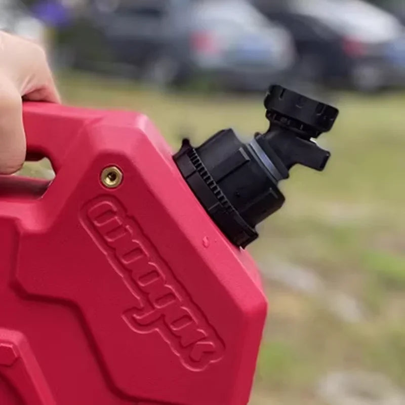 A hand holds a red universal fuel can with a black water tap adapter, set against a blurred outdoor background.