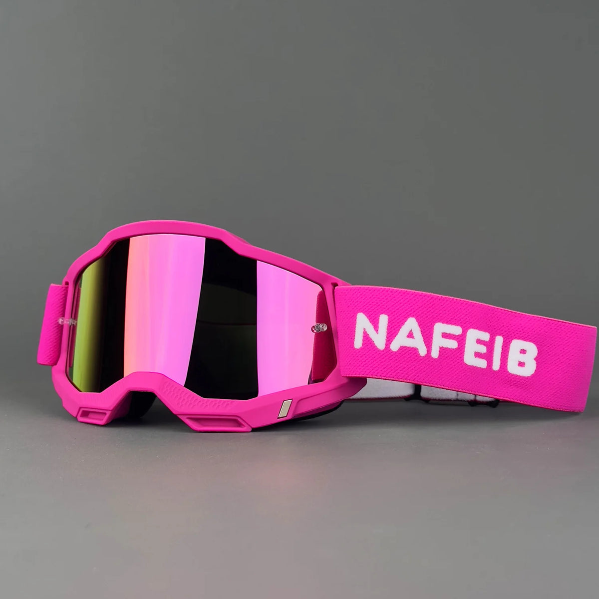 Pink off-road racing goggles with a strap and mirrored lenses resting on a gray surface.