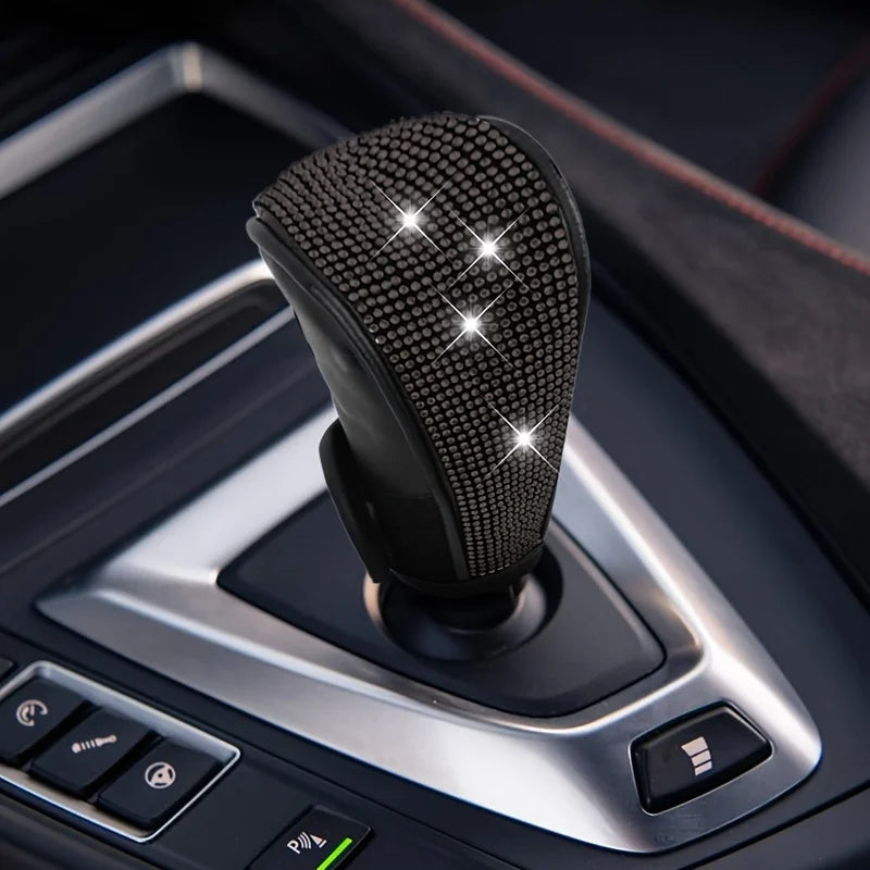 A close-up of a black gear shift knob cover with sparkling rhinestones, mounted in a car's center console.