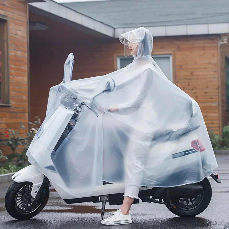 A person wearing a transparent windproof motorcycle rain poncho is sitting on a white scooter outdoors.