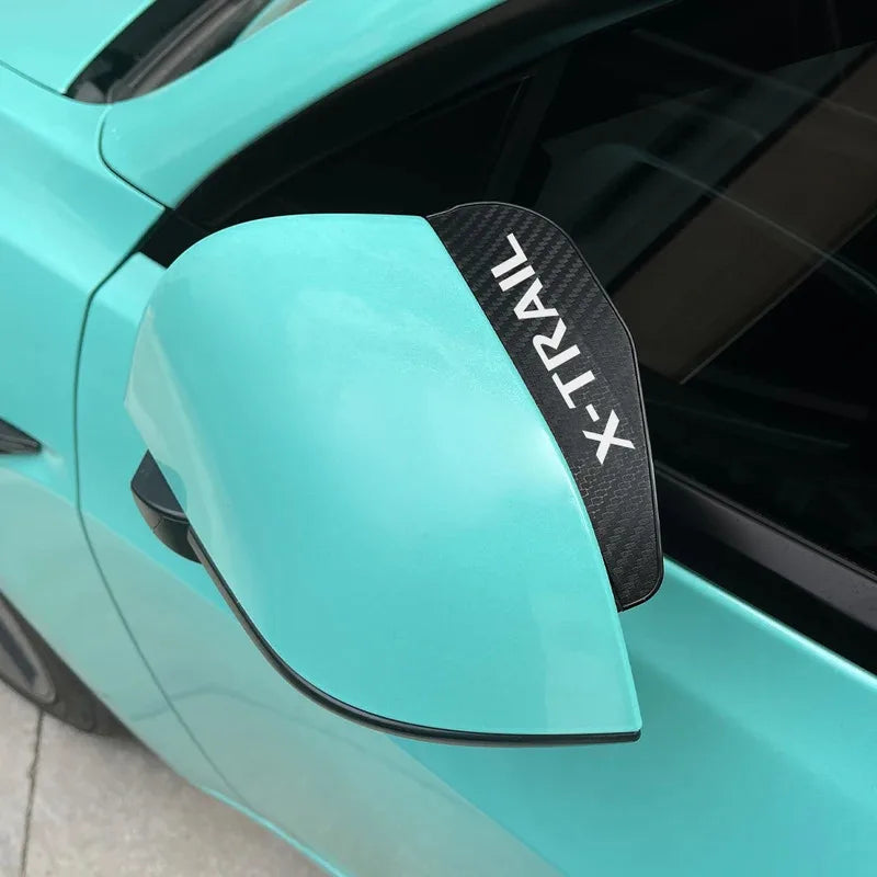 Close-up of a teal car's rearview mirror with an X-Trail eyebrow cover visible.