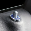 A silver car door lock pin trim set with a textured cylindrical piece and blue gemstone accents resting on a dark leather sur