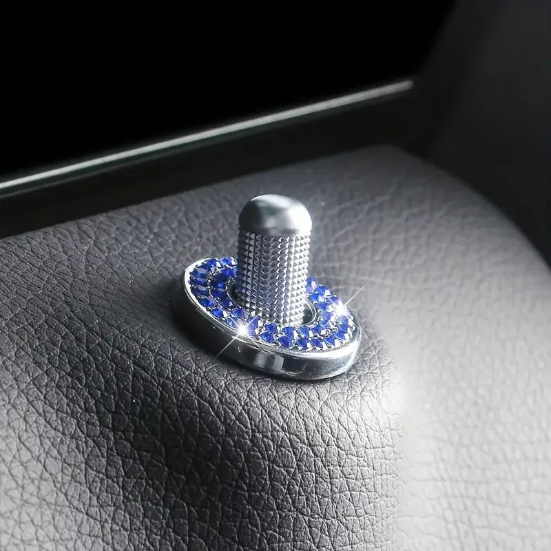 A silver car door lock pin trim set with a textured cylindrical piece and blue gemstone accents resting on a dark leather sur