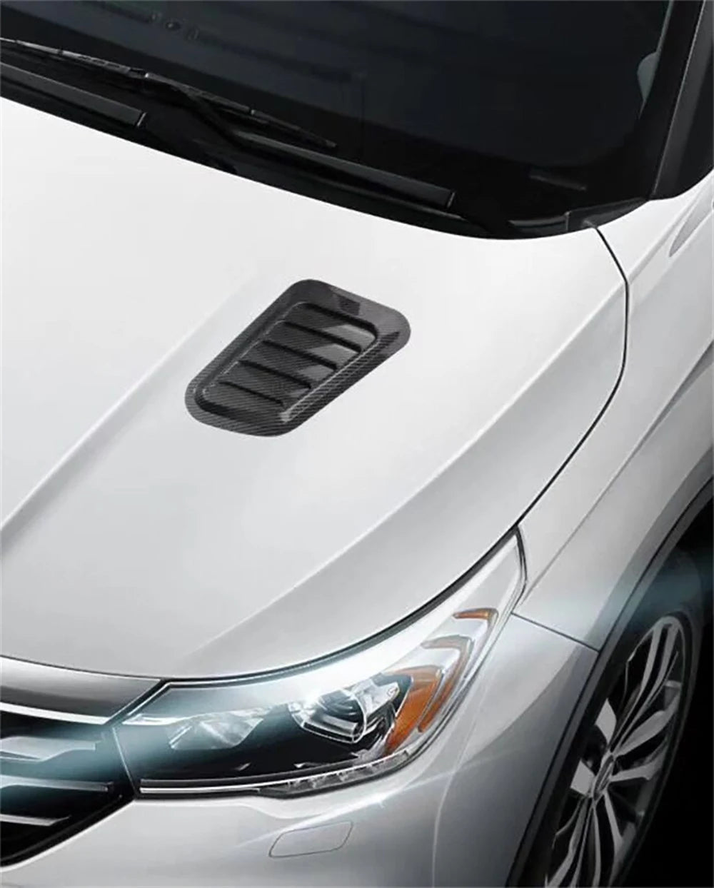 Carbon fiber hood scoop vent trim on a white car's front fender.