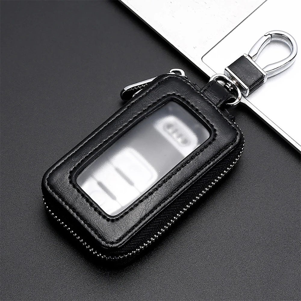 A black leather key protector pouch with a clear window and silver clasp resting on a dark surface.
