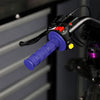 Close-up of black silicone handle bar grips with purple and yellow accents mounted on a motorcycle handlebar.