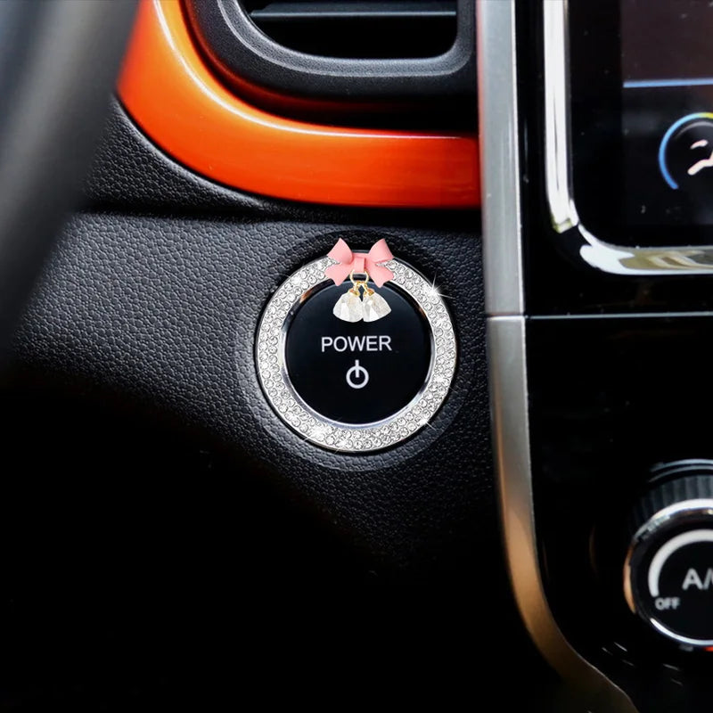 Close-up of a car start switch button featuring a rhinestone bow bell decoration.