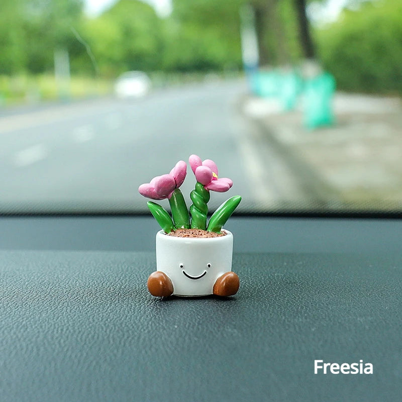 Kleine weiße Harz-Elf-Auto-Dekoration in Form eines lächelnden Gesichts, das rosa Freesienblumen hält.