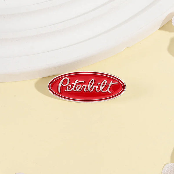 A red oval enamel lapel pin featuring the Peterbilt logo on a light yellow background.
