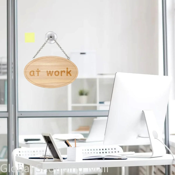 Un letrero de madera con las palabras 'at work' colgando en una división de vidrio en un entorno de oficina.