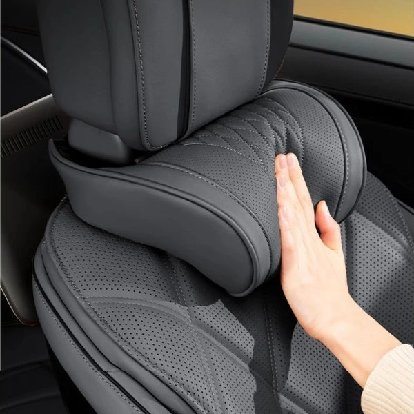 A hand is adjusting a gray leather car neck pillow inside a car seat.