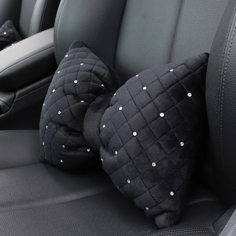 A set of black quilted fabric car neck pillows adorned with small silver rhinestones resting on a dark gray car seat.