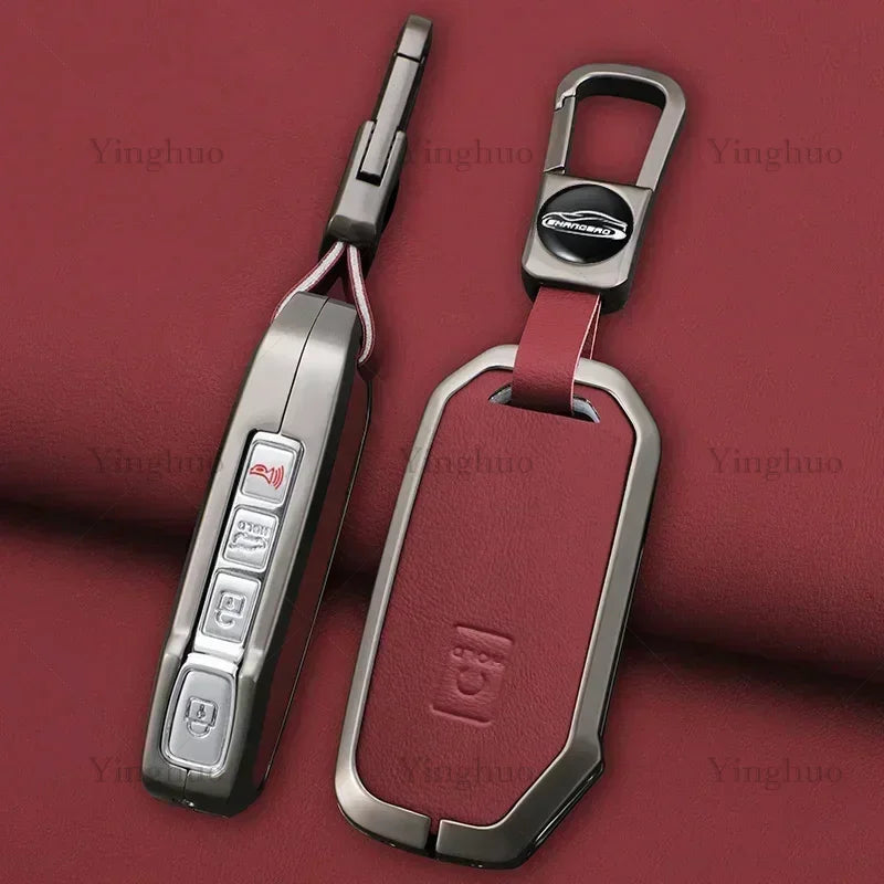 A silver key fob cover with a maroon strap and a metal keyring is shown against a dark red background.
